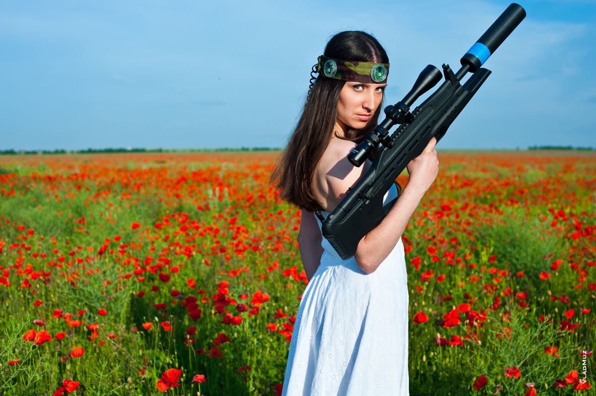 Фото девушки с лазертаг-винтовкой на фоне красного макового поля