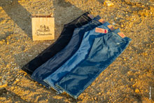 Фото 4-х джинсовых брюк и бумажного пакета с логотипом Woodcutter на фоне желтого грунта карьера