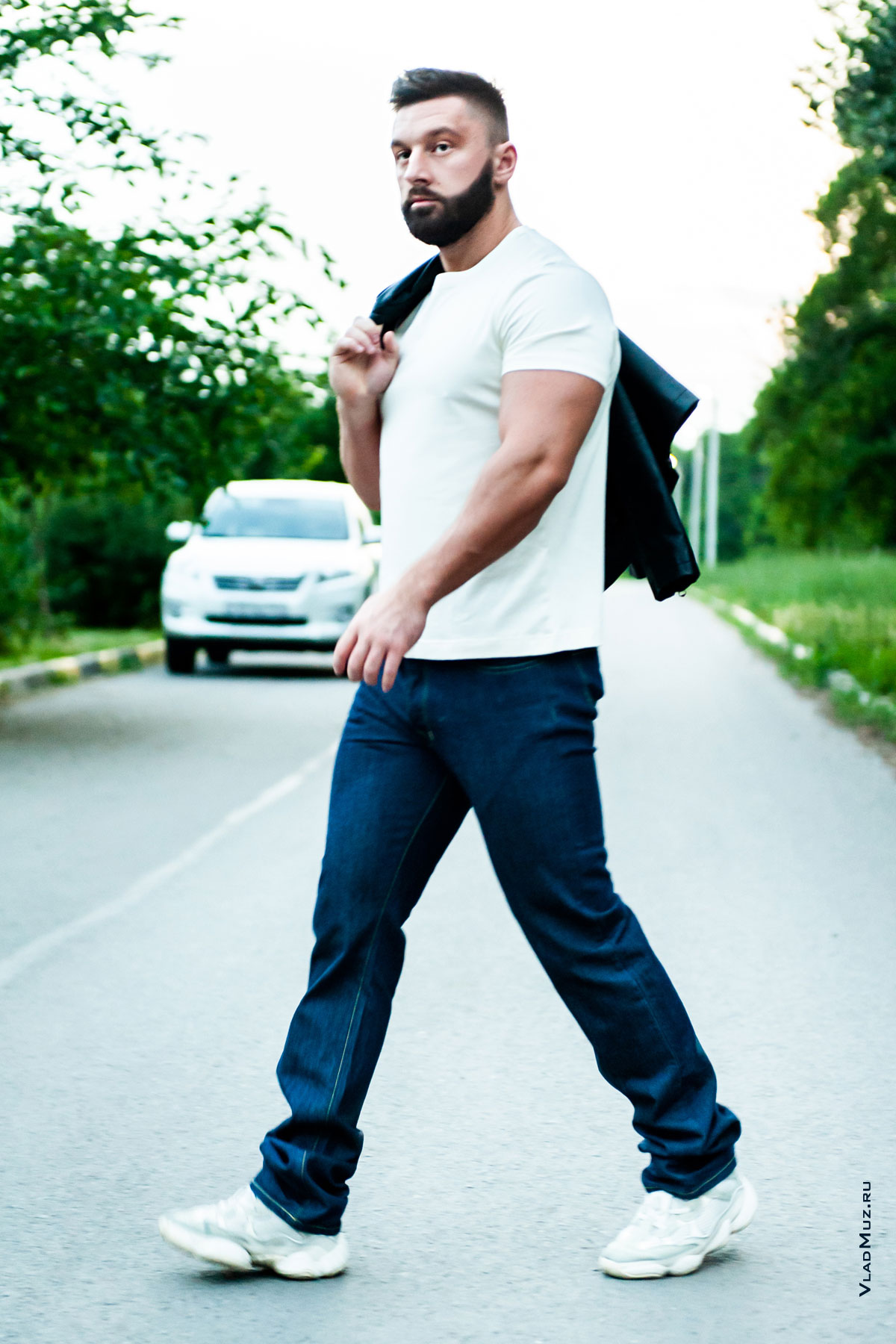 Фото идущего мужчины в полный рост в джинсах и футболке на фоне города
