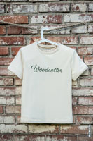 Фото бежевой футболки с надписью Woodcutter на фоне грубой кирпичной стены