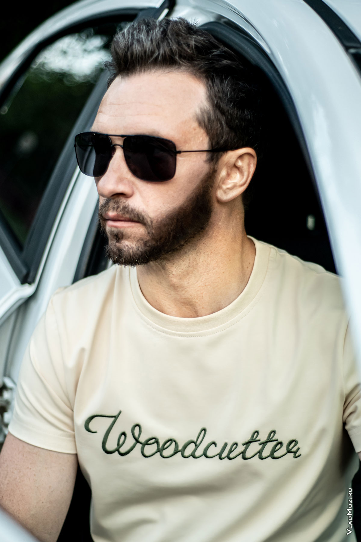 Рекламное фото мужчины в солнцезащитных очках и светло-бежевой футболке Woodcutter, сидя в автомобиле