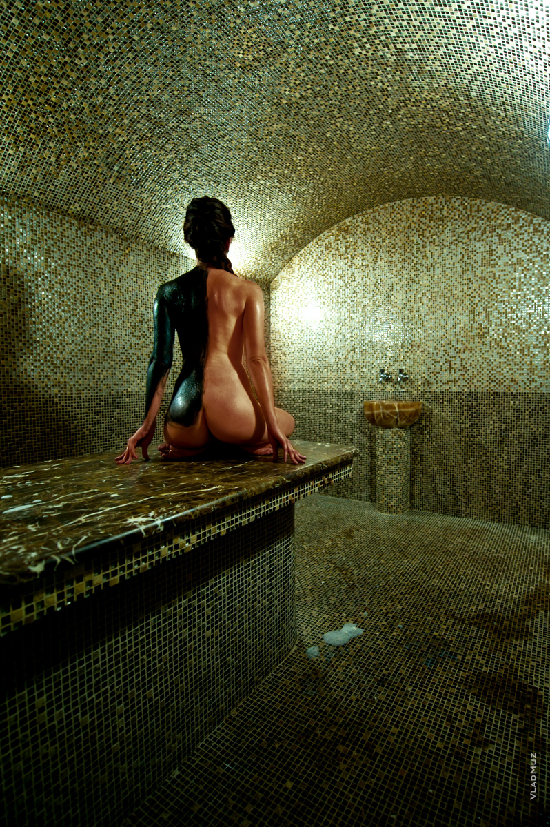 Эротическое фото обнаженной девушки в хамаме со спины, наполовину обмазанной черной глиной