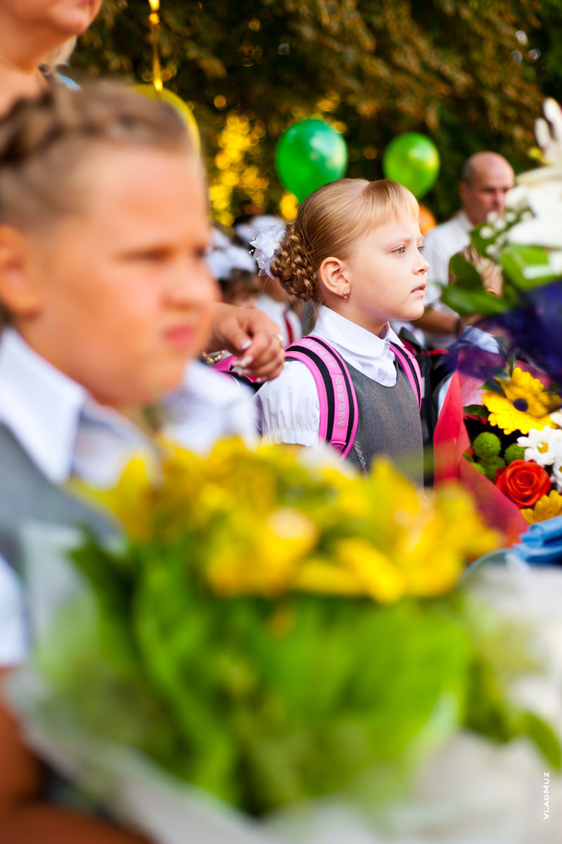 Фото первоклассницы с избирательной резкостью среди одноклассников и цветочных букетов