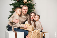 Семейный фотопортрет с подарками у новогодней елки в студии на белом фоне