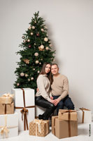 Парный фотопортрет мужчины и девушки у новогодней елки с подарками в студии на белом фоне
