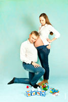 Фото беременной девушки стоя, будущий отец прислушивается к животу, стоя на колене