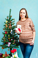 Фото девушки в вязанном свитере рядом с новогодней елкой с плюшевой игрушкой в руках