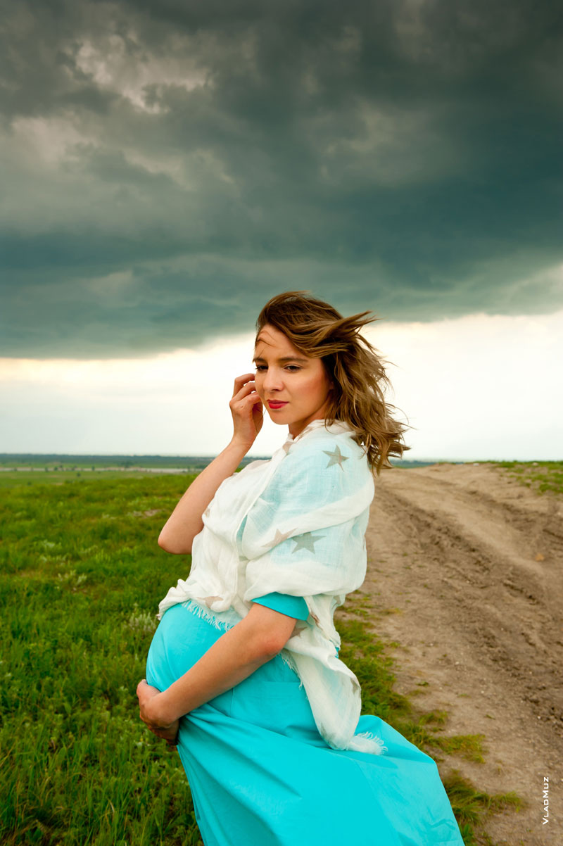 Фотопортрет беременной девушки в бирюзовом платье на фоне грозового неба