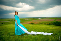 Фото беременной девушки в поле, на фоне грозового неба, с белой тканью в руке