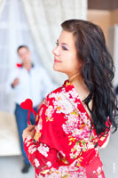 Красивый фотопортрет девушки в красном платье на фоне мужчины, стоящего вдали, в расфокусе