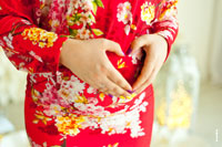 Фото рук беременной в форме сердца на животе, на фоне красного платья