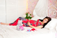 Фото беременной жены на кровати, рядом голубые пинетки и мягкая игрушка медведя
