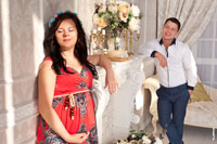 Семейное фото в интерьере фотостудии: беременная жена в лучах солнца и муж рядом с улыбкой