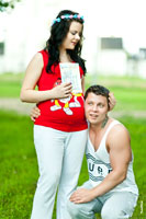 Семейное фото на природе: муж прислушивается к животу беременной жены, у которой в руках открытка мужу