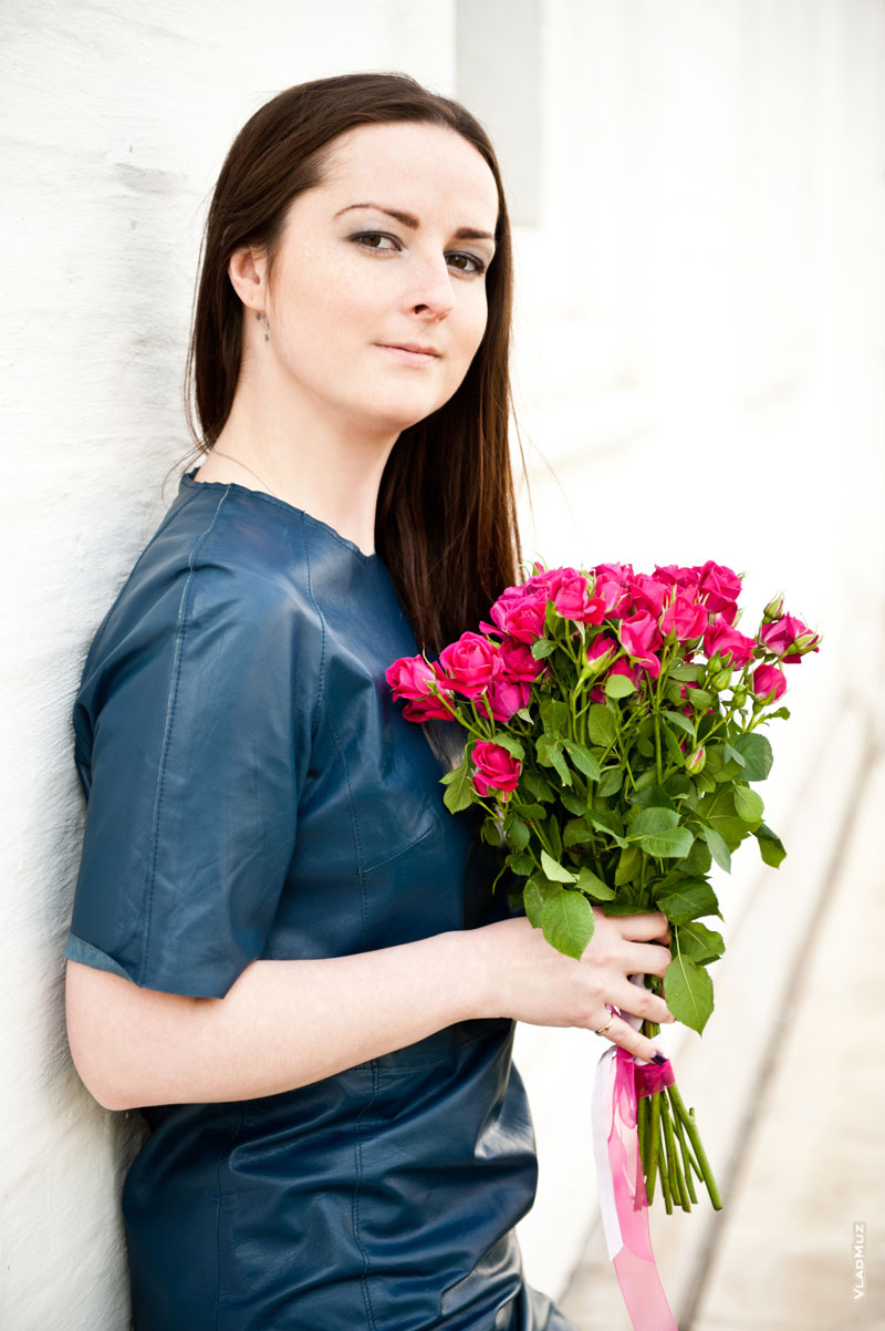 Фотопортрет девушки у белой каменной стены с букетом алых роз