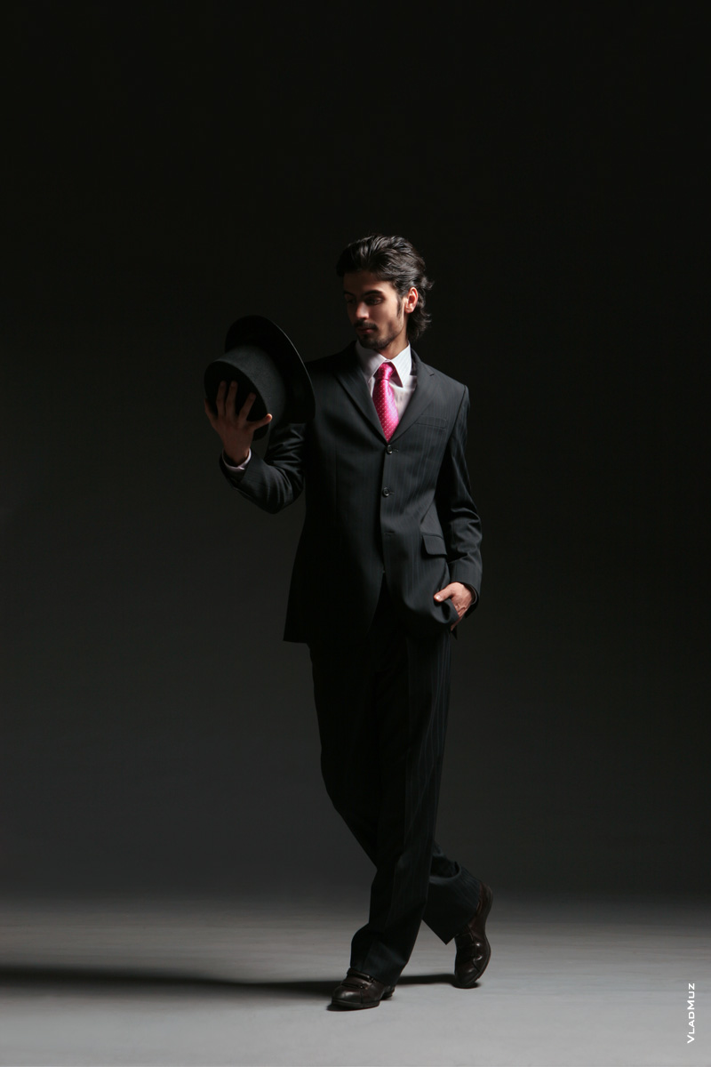 Фото мужчины-модели в темной тональности (на темном фоне) в полный рост с цилиндром в руке