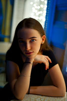 Фотопортрет девушки с рукой у подбородка, сидя за столиком в кафе