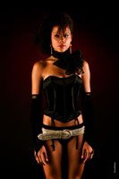 Поясной фотопортрет темнокожей девушки-мулатки в корсете на черном фоне