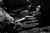 Черно-белое фото девушки в солнечных очках в воде среди камней