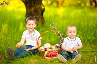 Фото детей на лужайке под деревом, с корзиной пасхальных куличей и клубникой