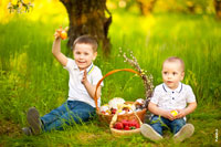 Детский парный фотопортрет 2-х мальчиков, играющих на лужайке под деревом с пасхальными яйцами