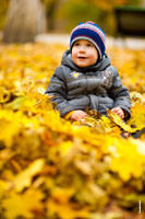 Осенний фотопортрет ребенка с улыбкой, сидящего в парке на желтых листьях