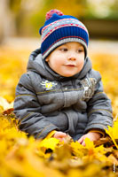Детский осенний фотопортрет мальчика в парке, сидящего на желтых листьях
