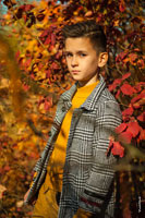 Модный детский осенний фотопортрет мальчика в пальто в лучах солнца на фоне из листвы