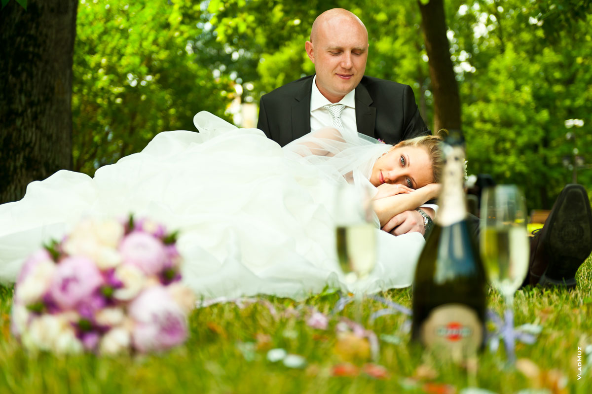 Фотопортрет невесты, лежащей на коленях у жениха, в расфокусах цветов и шампанского