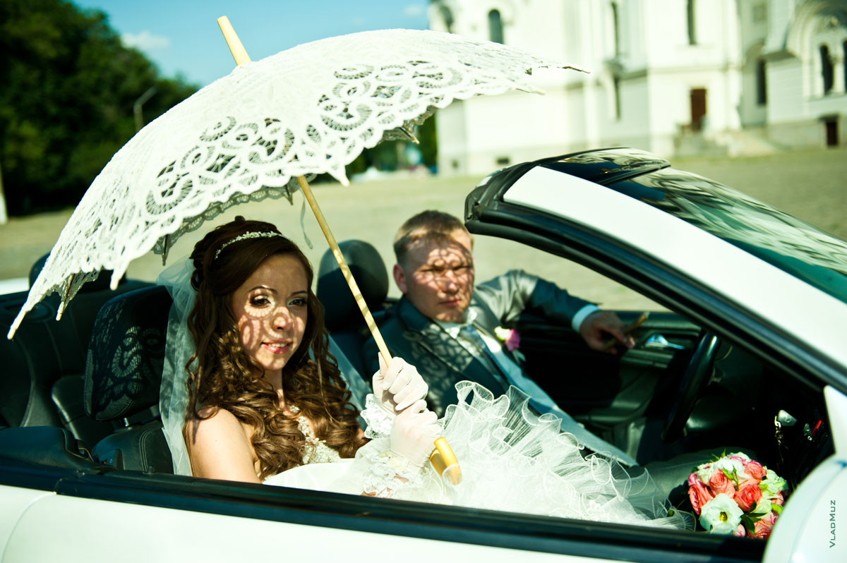 Жанровый свадебный фотопортрет невесты и жениха в кабриолете с оригинальным светотеневым рисунком на лицах