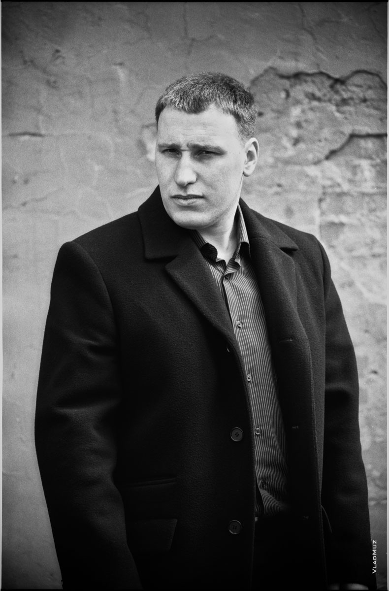 Жанровый черно-белый портрет мужчины в пальто, на улице, у стены