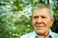 Горизонтальный фото портрет пожилого мужчины с избирательной резкостью на глазах на фоне цветущего дерева