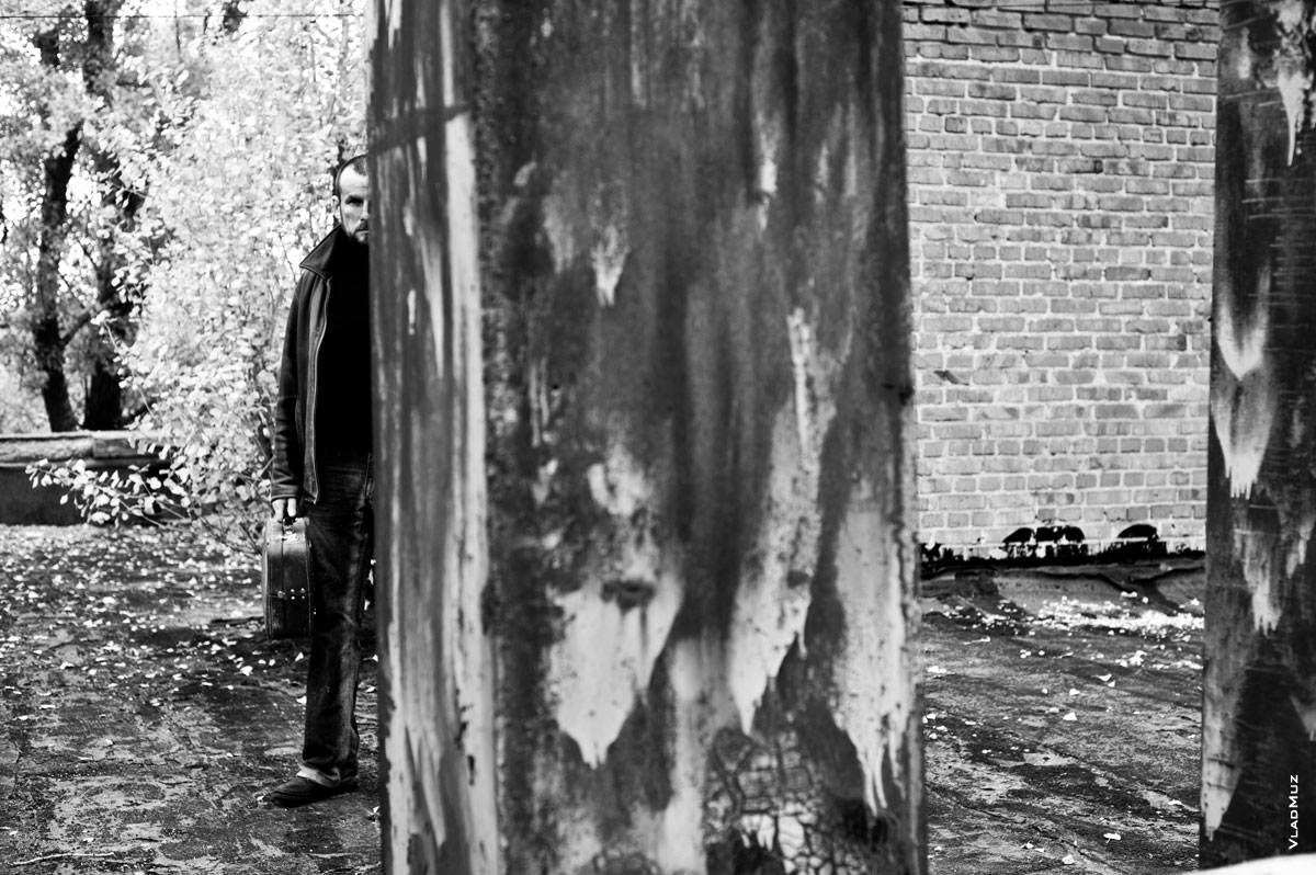 Черно-белое фото мужчины с чемоданом в руке, наполовину спрятавшегося за стеной