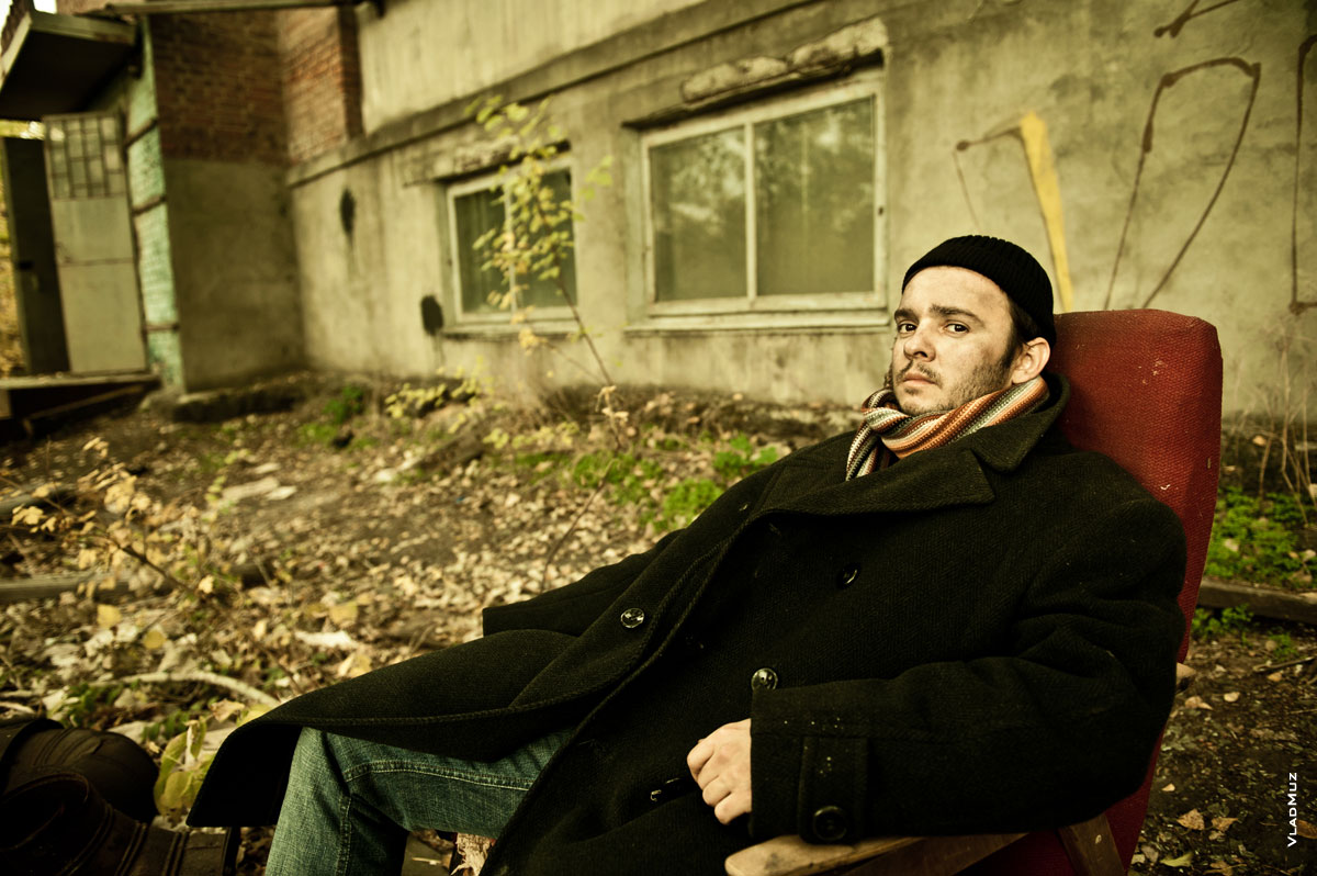 Жанровый портрет мужчины в кресле на улице, в черном пальто и шапочке