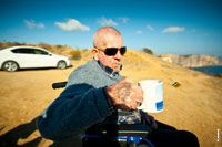 Жанровый фотопортрет мужчины в солнечных очках, с кружкой чая, с татуировкой на руке, на природном фоне