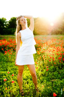 Летнее фото девушки-блондинки в белом платье на фоне макового поля в контровом солнечном свете