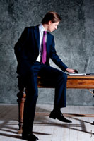 Фото делового мужчины в костюме, в полный рост, сидя на столе за ноутбуком