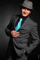Еще одна портретная фотография Андрея Разыграева в костюме, бирюзовом галстуке и в шляпе с улыбкой настоящего шоумена