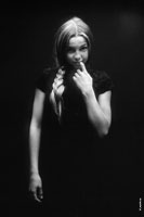 Фотопортрет смущенной девочки с пальцем во рту на черном фоне, в темной тональности