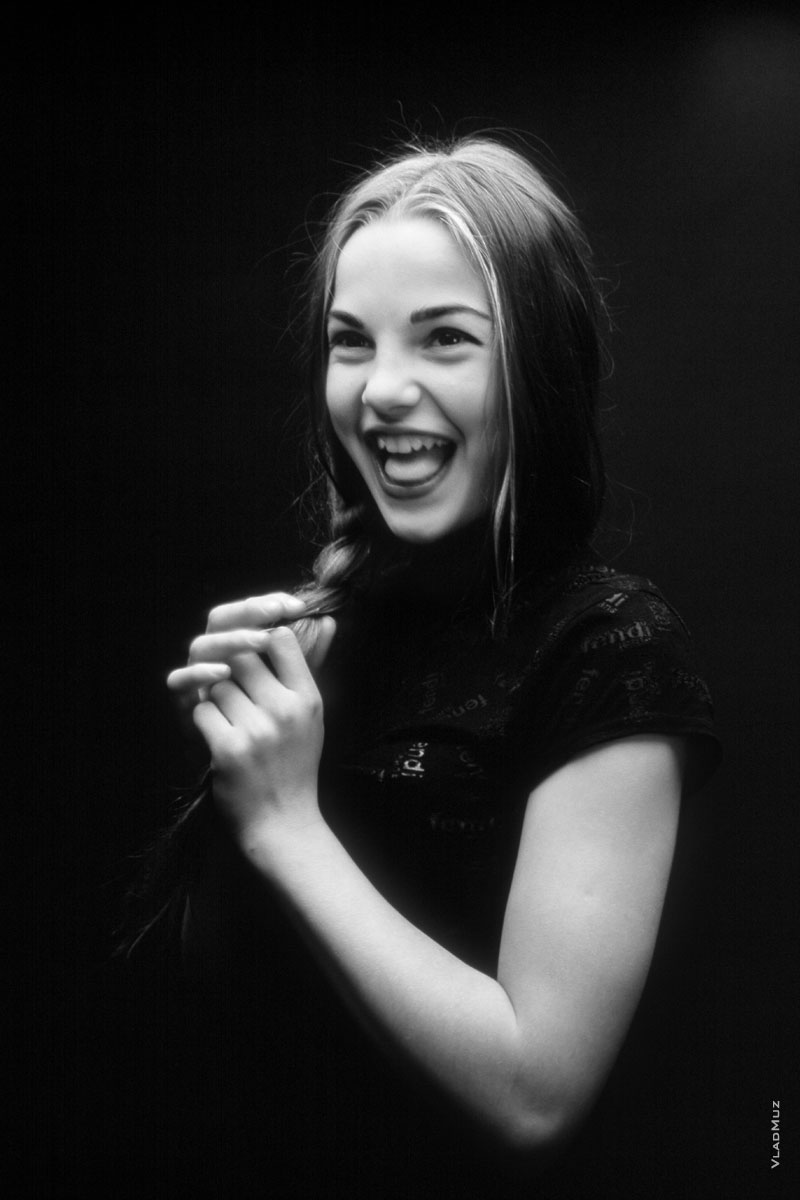 Фотопортрет озорной, смеющейся девочки на черном фоне в темной тональности