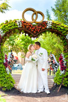 Фото молодоженов в свадебной сердечной арке с кольцами вверху