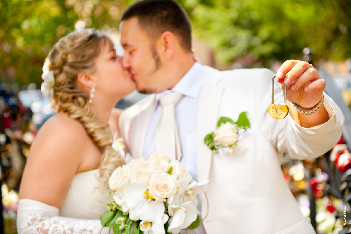 Свадебный замочек в фокусе, жених с невестой и их свадебный поцелуй — в расфокусе