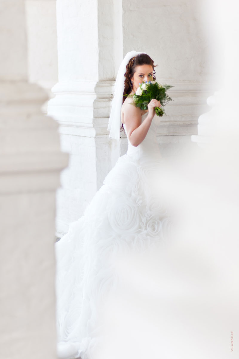 Фото невесты с букетом на фоне белых стен и арок храма Вознесения Господня в Коломенском