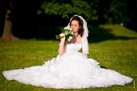 Фото невесты с букетом, сидящей на лужайке, и большого свадебного платья