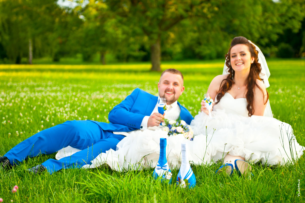 Веселое фото свадебной пары на лужайке с бокалами шампанского