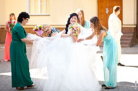 Подружки невесты чистят свадебное платье. Невеста смеется