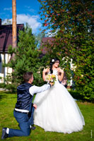 Фото на лужайке: жених перед невестой на колене с букетом, невеста в восторге