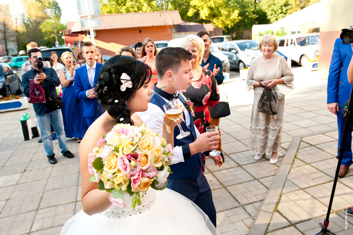 Жених с невестой традиционно пьют перед входом в ресторан шампанское из бокалов