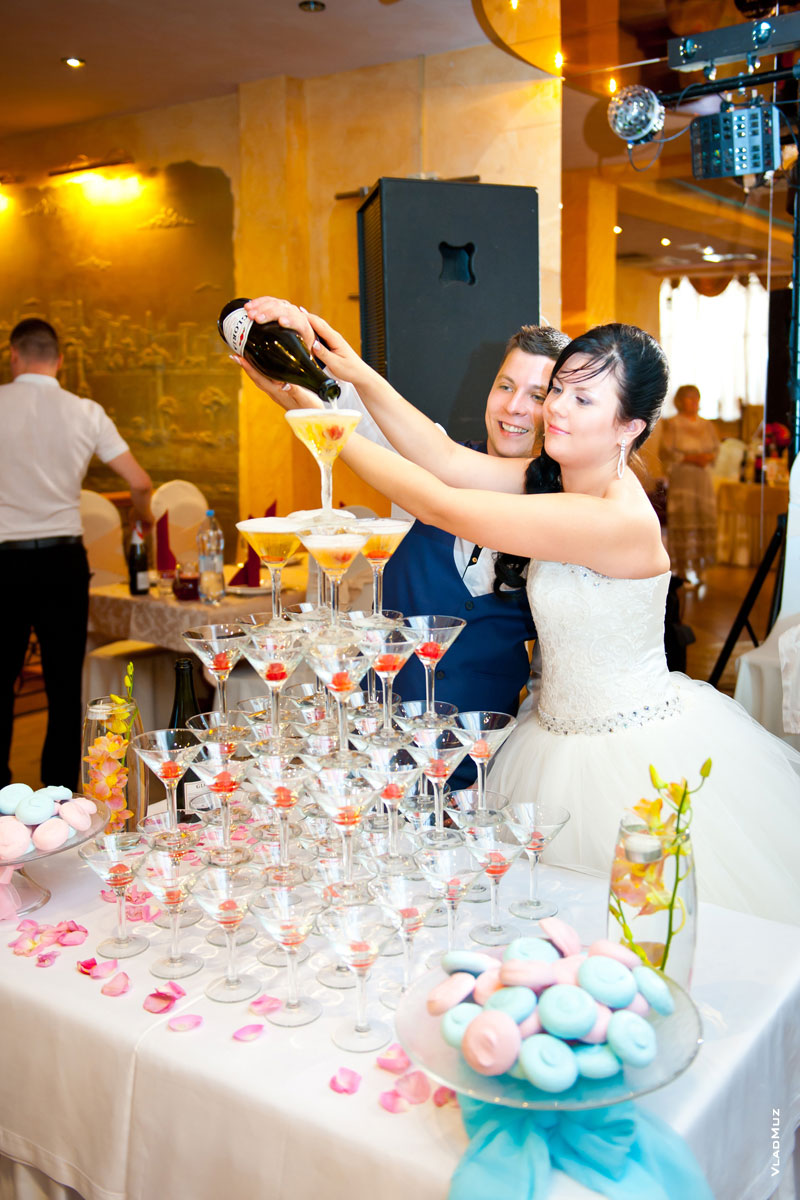 Жених с невестой наполняют в ресторане шампанским пирамиду из бокалов