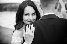 Черно-белый фотопортрет невесты с акцентом на глазах и кольцом на руке, жених стоит спиной в кадре